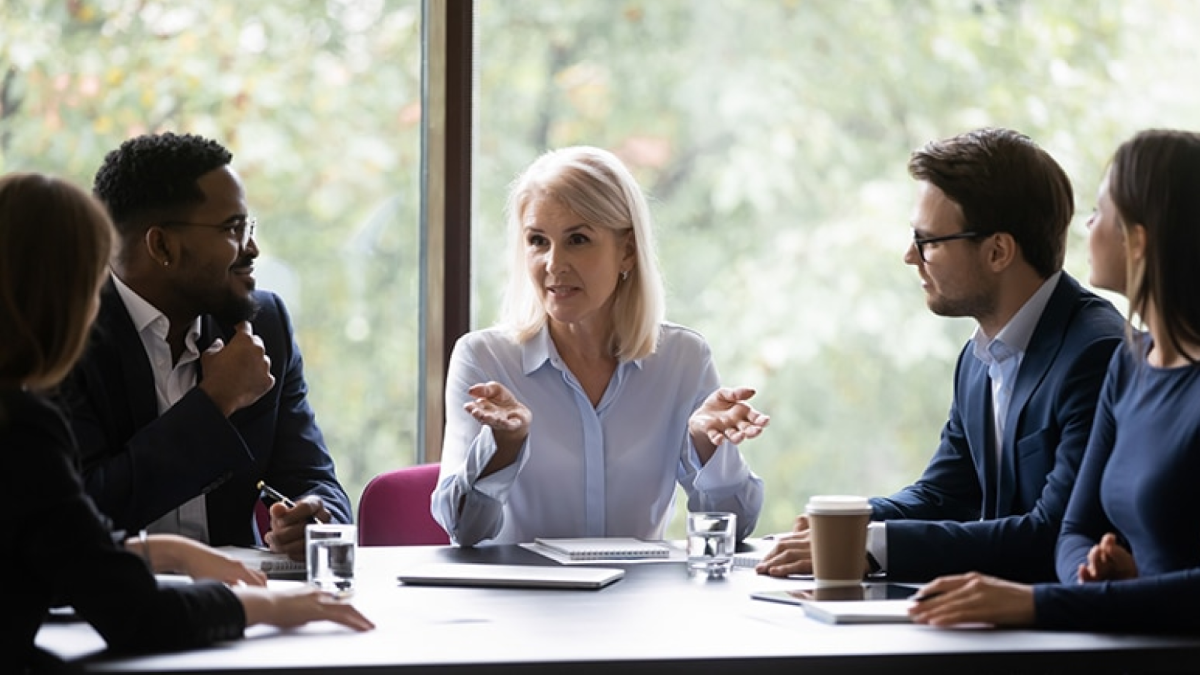 A woman sits at a table and explains a presentation to people sitting on either side of her.