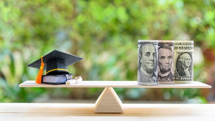 A scale is shown with a graduation cap and diploma on the left side and three rolls of U.S. currency shown on the right.