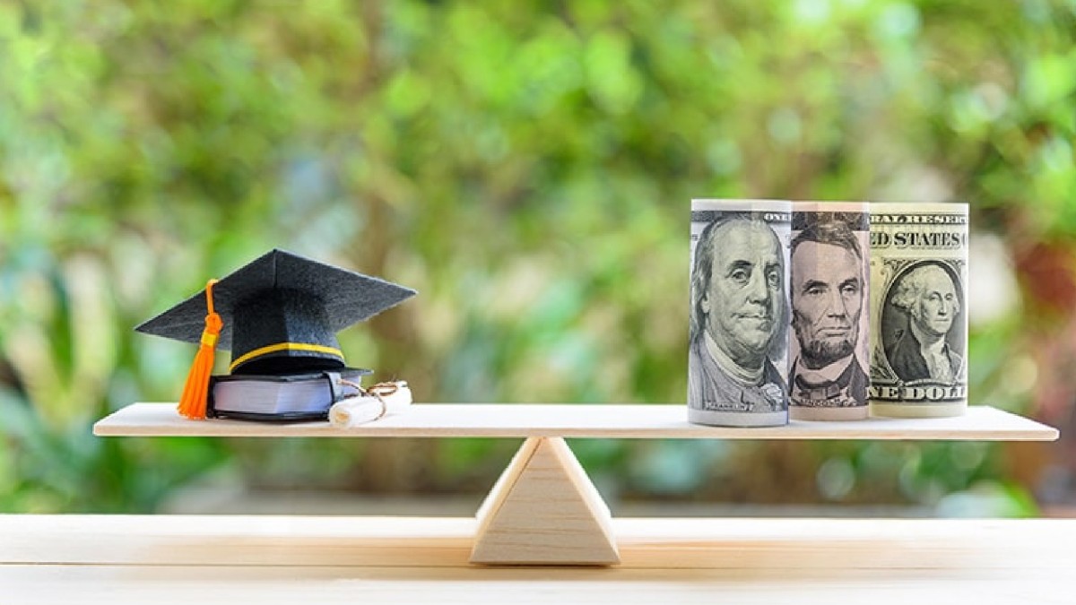 A scale is shown with a graduation cap and diploma on the left side and three rolls of U.S. currency shown on the right.