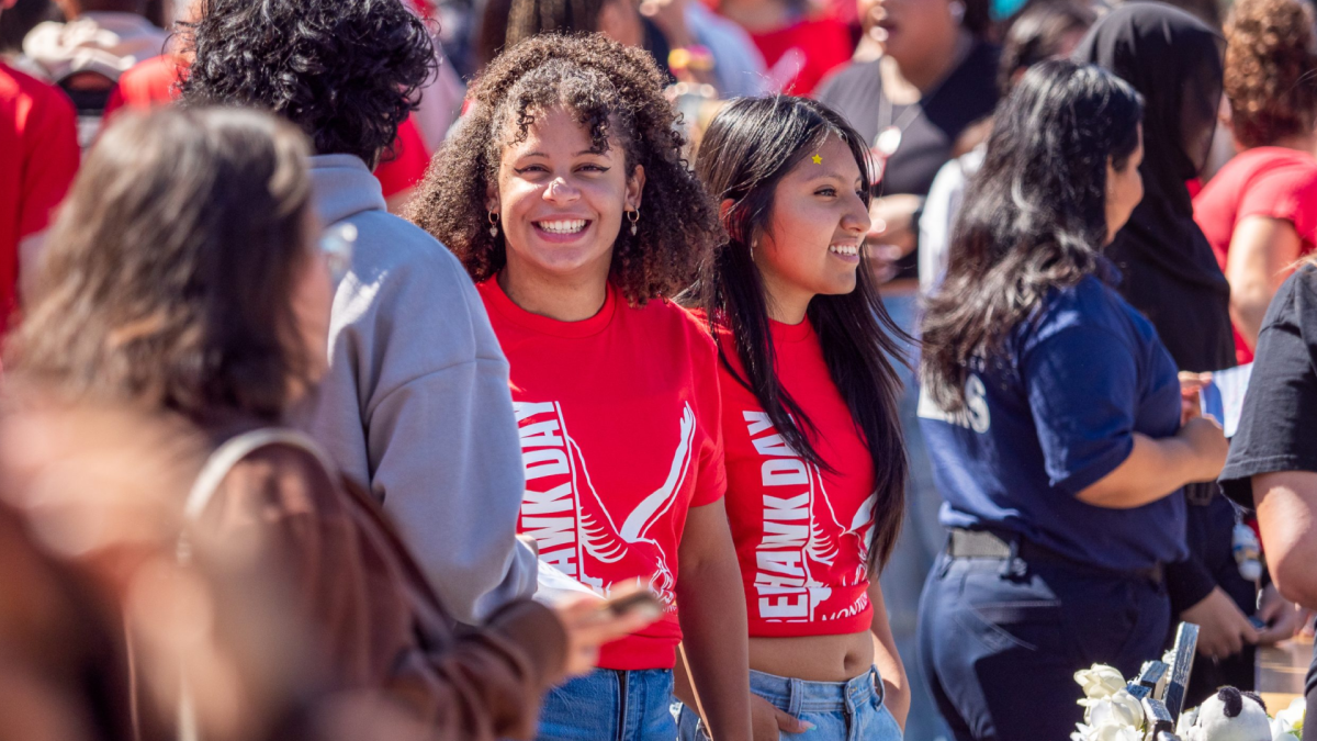 Students from diverse backgrounds gather at a university organization fair, wearing matching shirts and smiles.