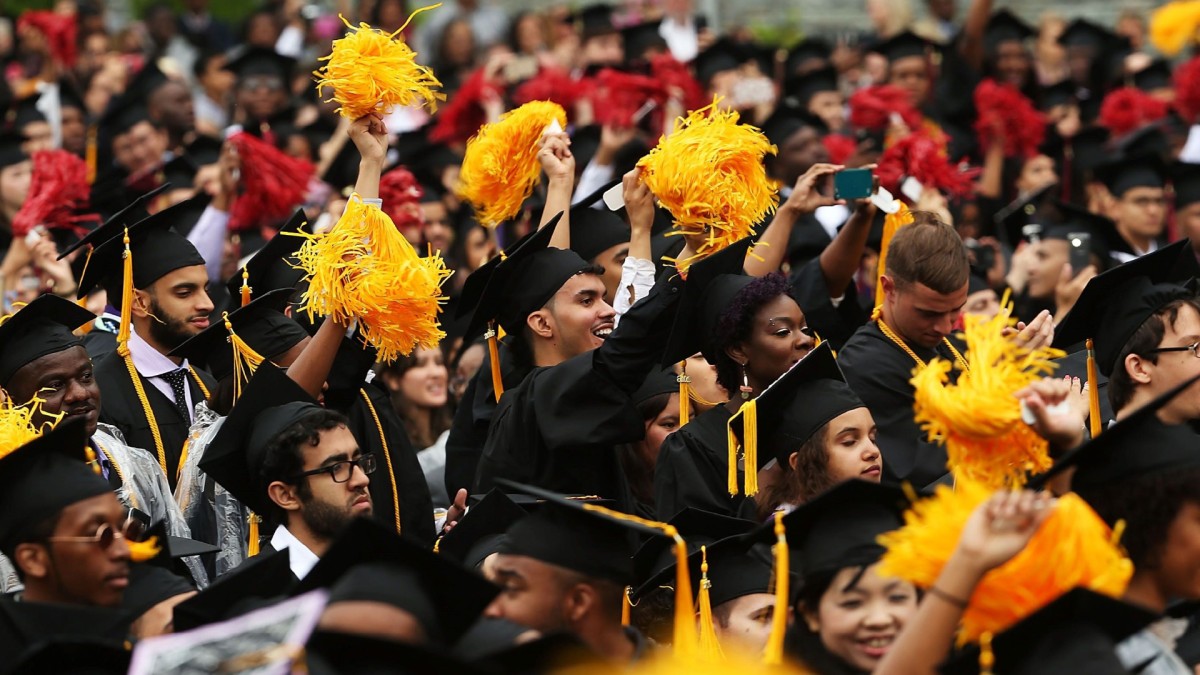 A crowd of graduating college students in caps and gowns shaking yellow pom poms.