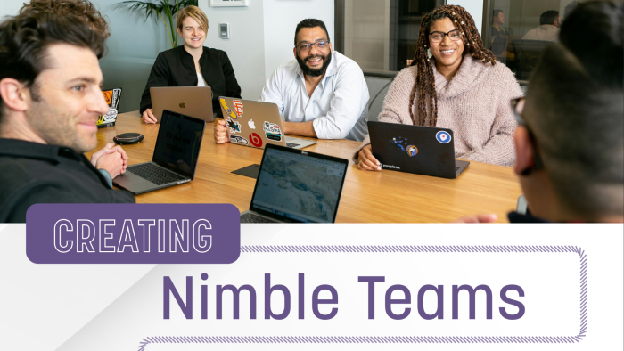 Four people with laptops sit at a table, listening to a presentation at work with the text “Creating Nimble Teams” displayed.