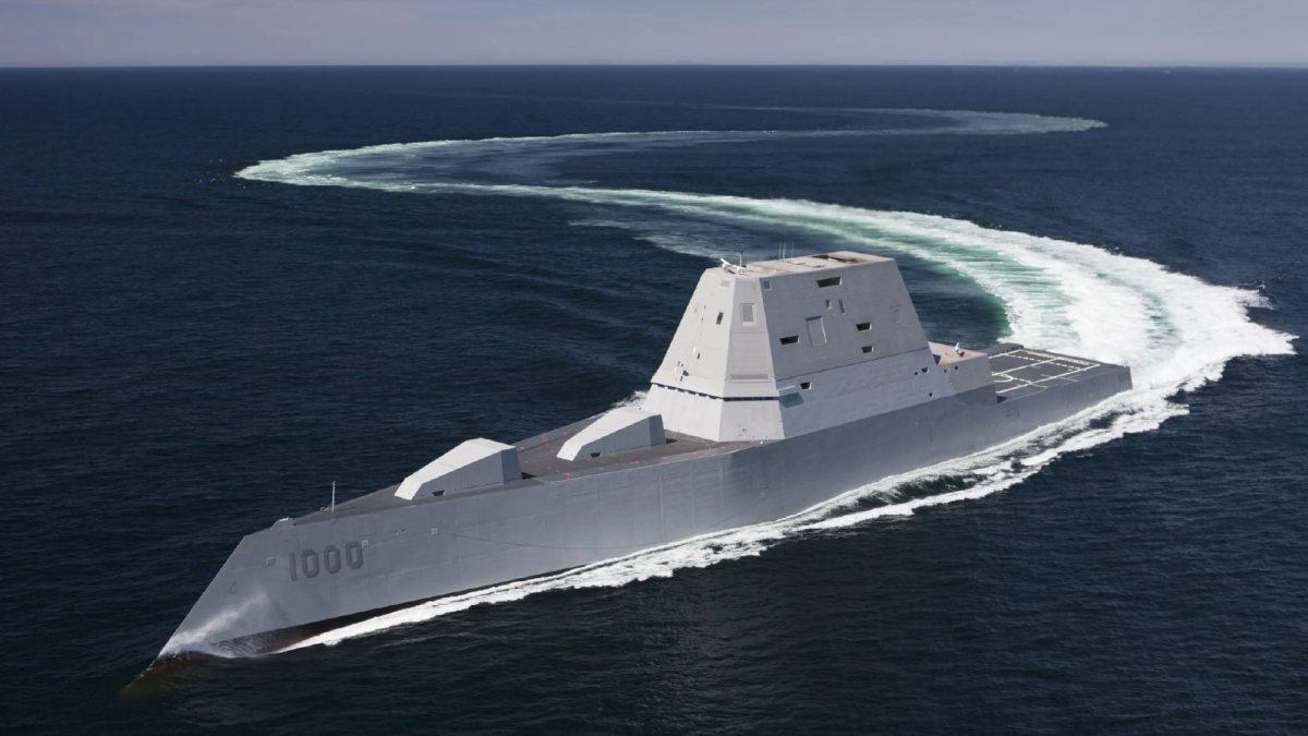 An iron-gray missile destroyer glides through the ocean, leaving white foam in its wake.