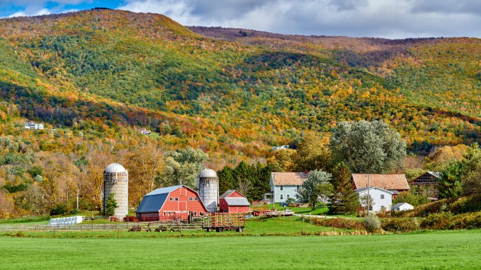 A red barn, two silos, a house, and assorted farm buildings nestled within a hilly autumn landscape.