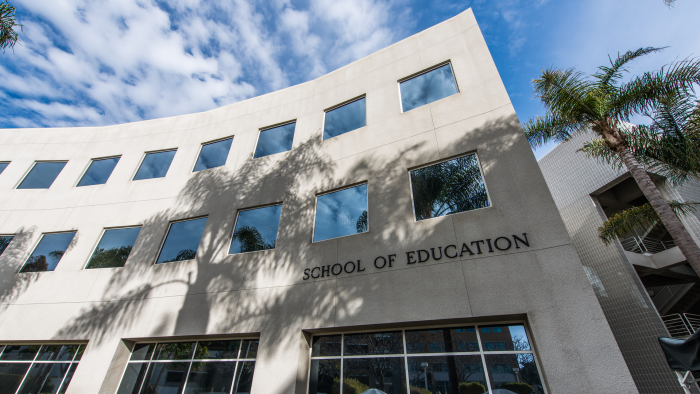 A gray School of Education building on a college campus in California with blue sky in the background