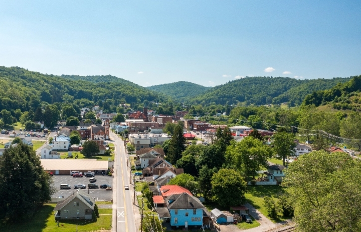 An aerial view of a small village nestled between tree covered hills.