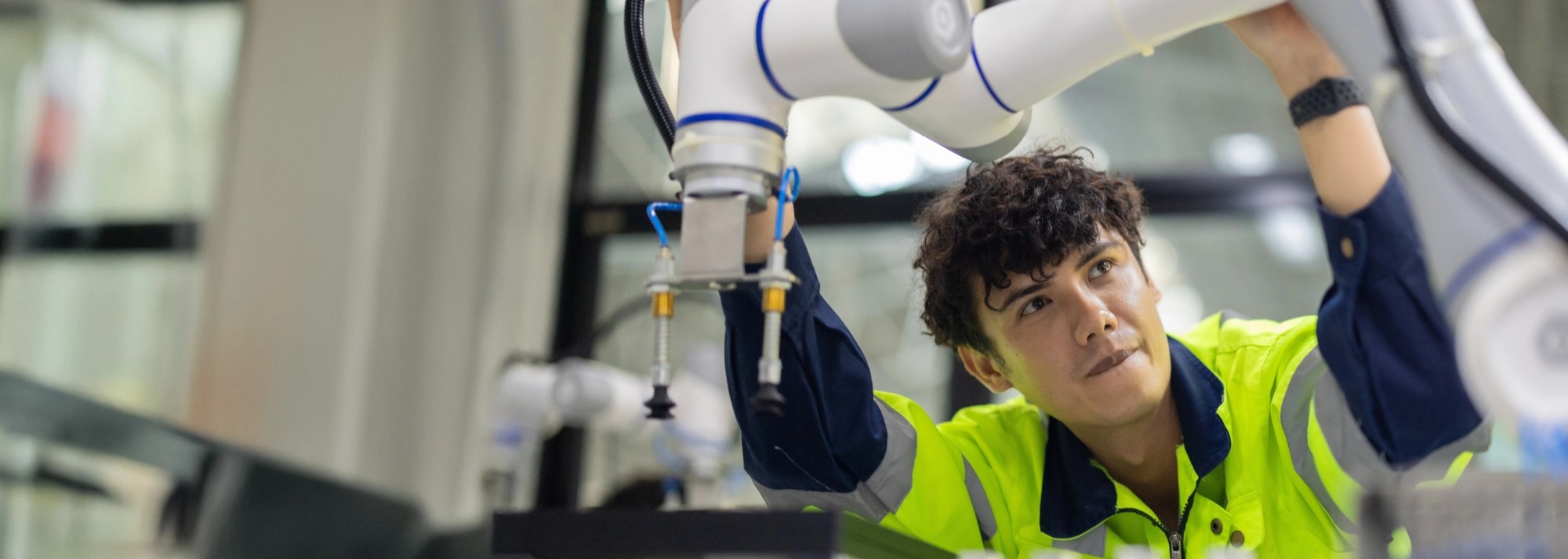 A young man in a fluorescent safety vest makes adjustments to a large white robotic arm