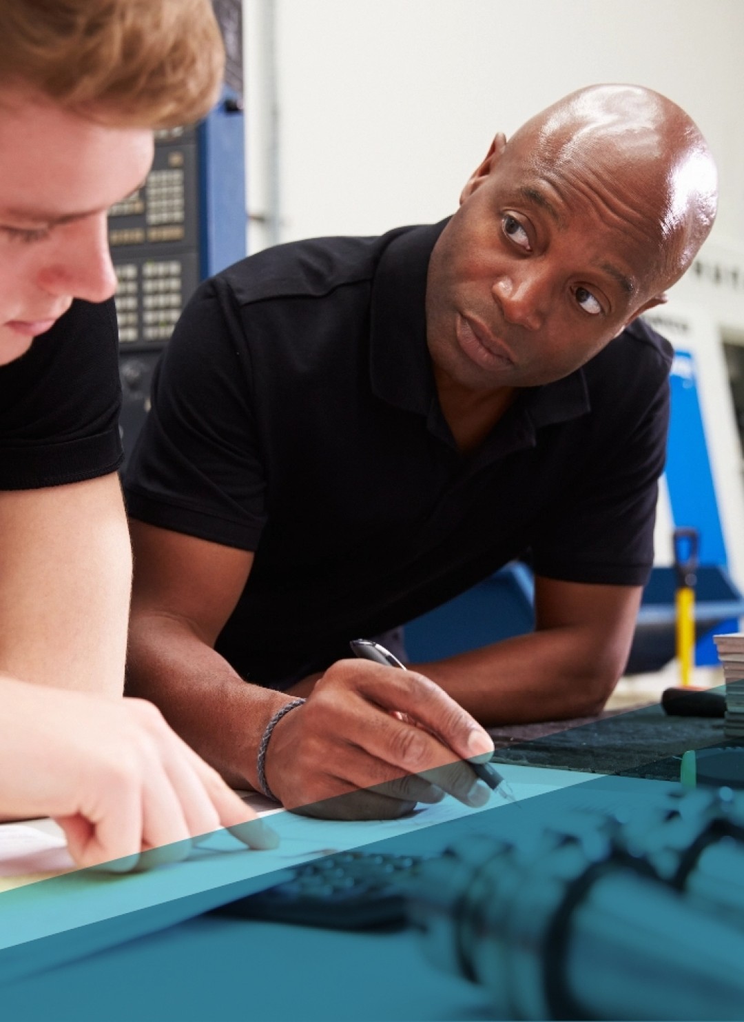 And older black man with a bald head holding a pen looks expectantly at a young white man who is pointing and looking down at printed material.