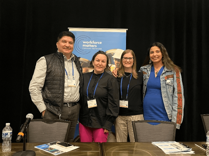 Four members of Workforce Matters’ advisory committee stand in front of a banner during a conference.